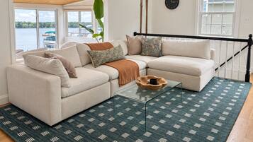 A living room with a sectional sofa, a glass coffee table, and a view of a lake.