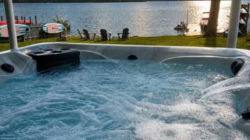 A hot tub with a view of a lake and chairs on the deck.