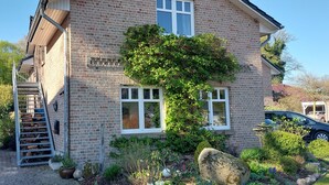 A brick house with a wooden staircase, a car parked in the driveway, and a garden with various plants.