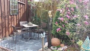 A wooden building with a patio area featuring a table and chairs, surrounded by plants and decorative elements.