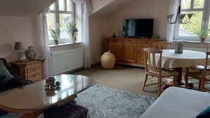 A cozy living room with a sofa, a glass-top coffee table, a dining table with chairs, a television, and potted plants. - Feldblick art oasis, near the heath and the Pietzmoor (Schneverdingen)