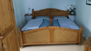 A wooden bed with a woven headboard, a bedside table with a lamp, and a vase on a small table.