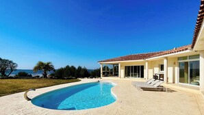 Ein Poolbereich mit klarem, blauem Pool, einer überdachten Terrasse und Blick auf das Meer.