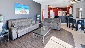 A modern living room with a gray sectional sofa, a glass coffee table, and a dining area with a dark wooden table and chairs. - Star Villa: Private Pool with 24/7 Support! (Davenport)