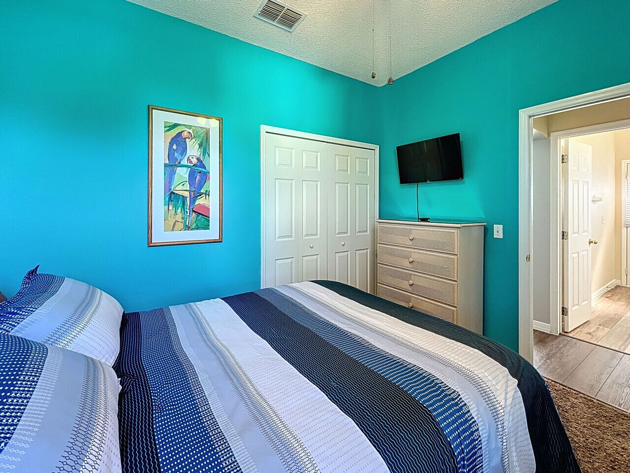 A bedroom with a bed, a dresser, a door, and a painting on the wall.
