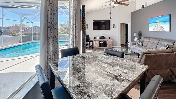 A modern living room with a marble dining table, leather sofas, a TV, and a pool view. - Star Villa: Private Pool with 24/7 Support! (Davenport)
