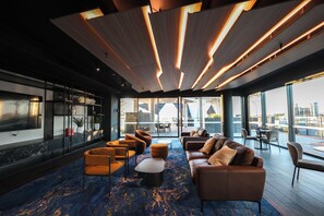 Ein moderner Lounge-Bereich mit großem Fenster, Sitzgelegenheiten und einer Holzkimpen-Decke.