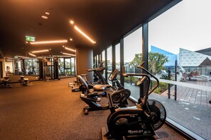 Ein Fitnessstudio mit Cardiogeräten, Gewichtsbänken und einem großen Fenster mit Blick auf die Stadt.