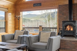 A cozy cabin interior with a fireplace, wooden walls, and a view of snow-capped mountains. - A modern log cabin with mountain views, hot tub, fire pit, vaulted great room. (Bailey)