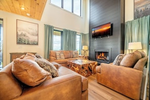 A modern living room with leather sofas, a wooden coffee table, a fireplace, and a TV mounted on the wall. - Spacious 4BD+Loft Near TOWN | Hot Tub +POOL +Sauna (Sevierville)