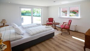 Un dormitorio con cama, dos sillas, una mesita y ventana con vista a la vegetación.
