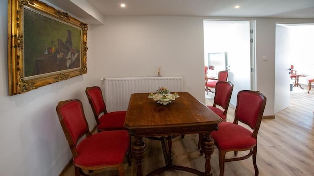 Un comedor con una mesa de madera y seis sillas tapizadas rojas. Un cuadro enmarcado cuelga de la pared sobre la mesa.