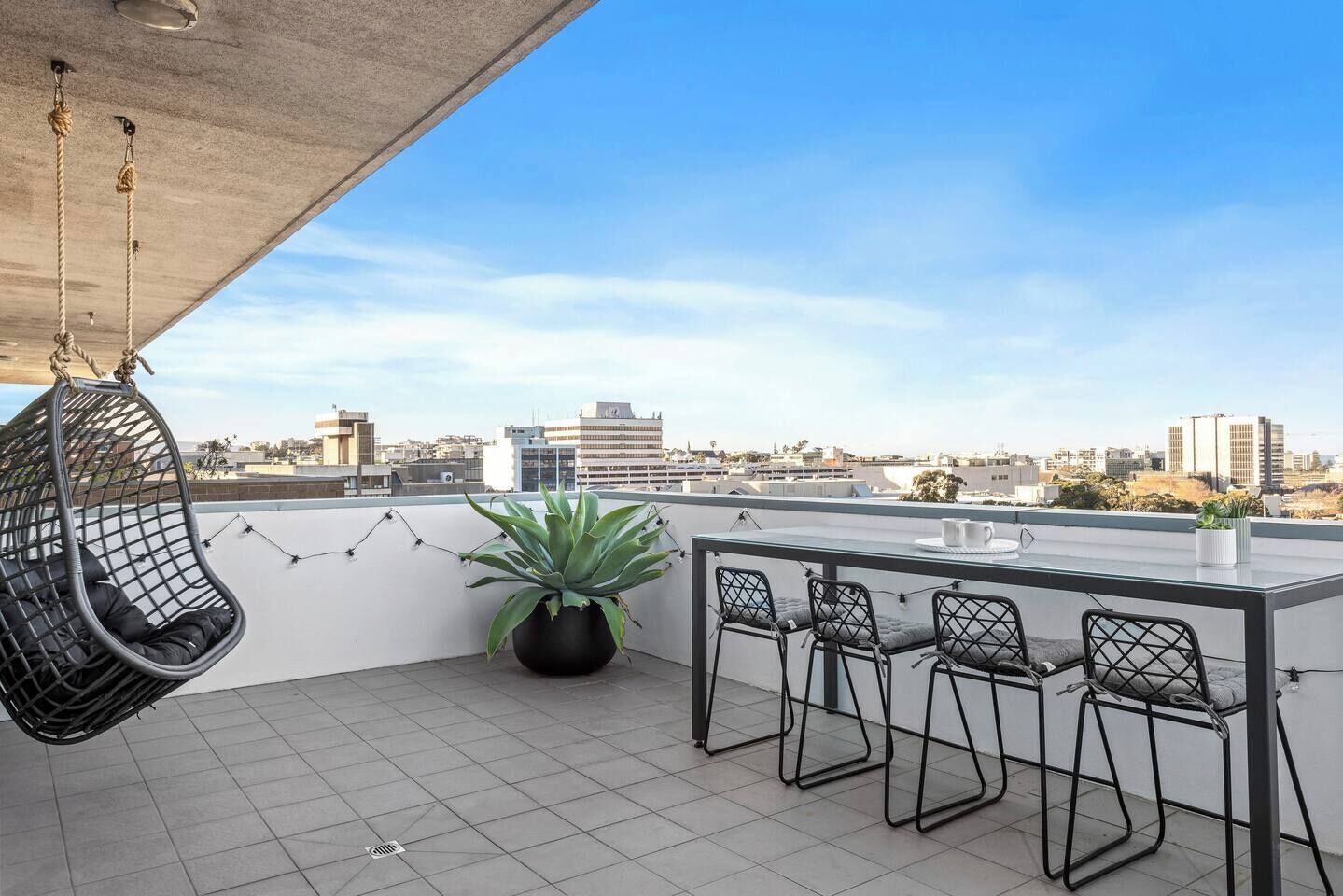 A rooftop terrace with a hanging chair, a potted plant, and a bar area with stools.