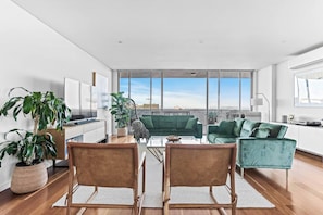 A spacious living room with a large window, a green sofa, a coffee table, and two chairs. - City Perch Escape Sweeping Penthouse style Haven (Wollongong)