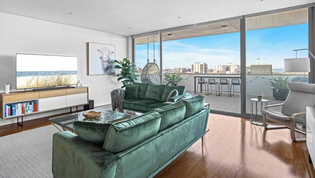 A modern living room with a green sofa, a flat-screen TV, and a large window overlooking a cityscape. - City Perch Escape Sweeping Penthouse style Haven (Wollongong)