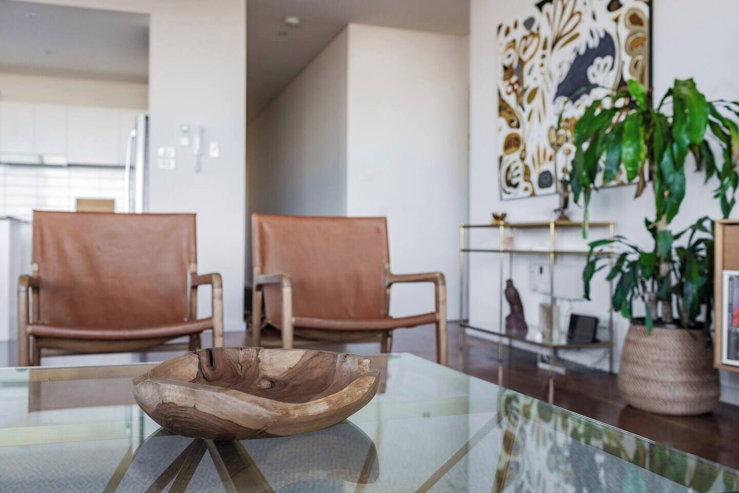 Een moderne woonkamer met twee leren fauteuils, een glazen salontafel en een grote potplant.