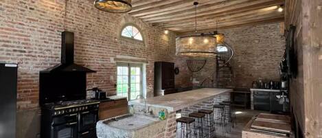 A spacious kitchen with exposed wooden beams, a brick wall, a large island with bar stools, and a built-in oven.