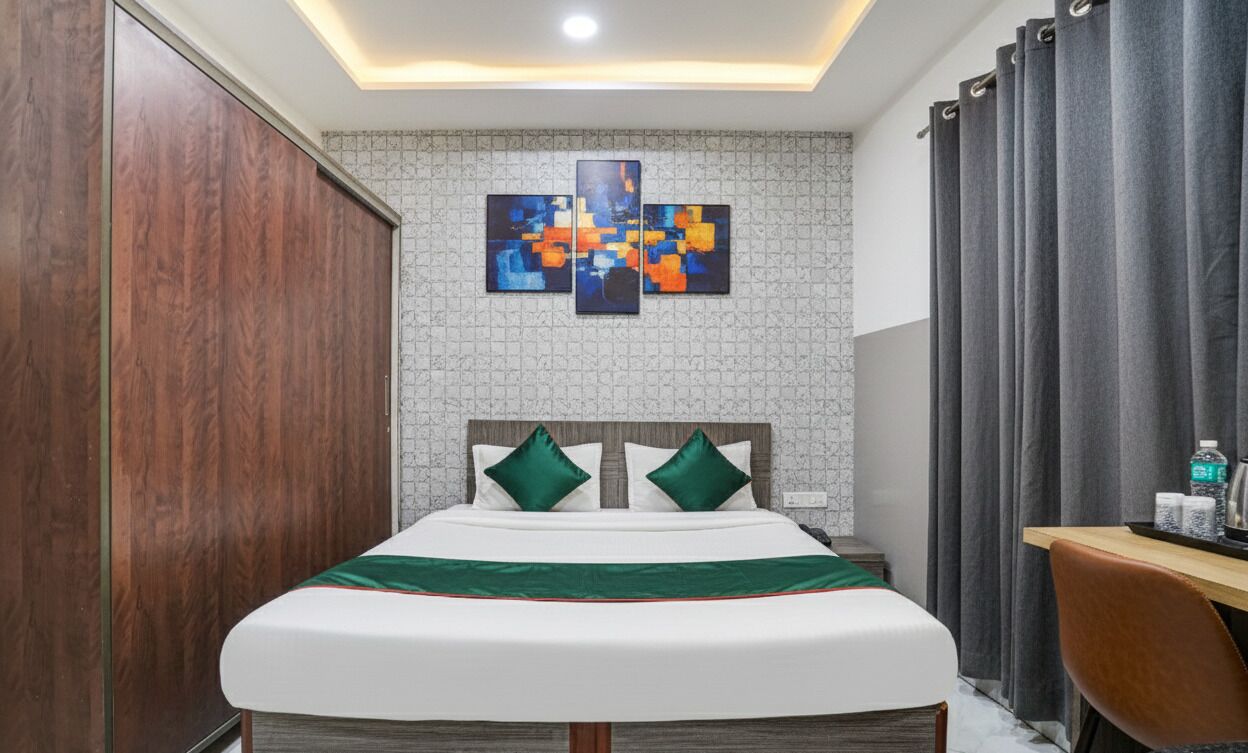 A hotel room with a bed, a wooden wardrobe, a desk, and a grey curtain.