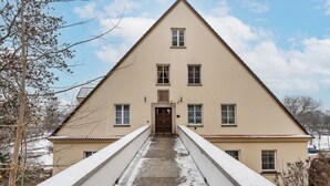 Ein symmetrisches Gebäude mit einem zentralen Eingang, das von zwei Symmetrie-Flügeln und einem mit Schnee bedeckten Dach flankiert wird.