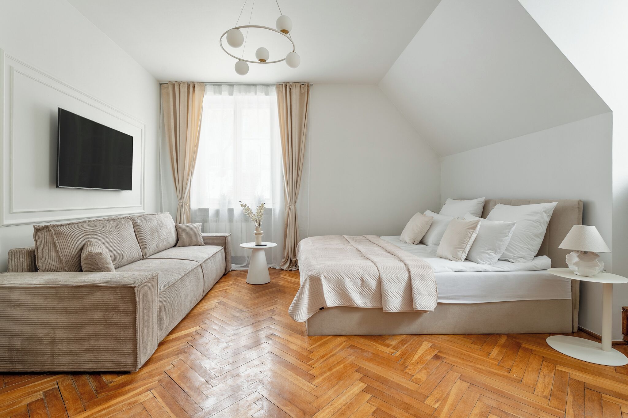 A modern bedroom with a sofa, a bed, a TV, and a small table.