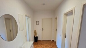 A hallway with white walls, a tiled floor, a round mirror, a white counter, and doors leading to other rooms. - Superior apartment with private balcony & parking space (Chemnitz)