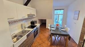A compact kitchen with white cabinets, a black stove, and a dining area with a table set for two. - Superior apartment with private balcony & parking space (Chemnitz)