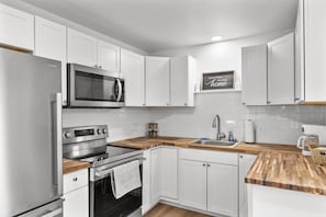 Une cuisine moderne avec des armoires blanches, des appareils en acier inoxydable et un plan de travail en bois.