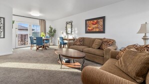 A living room with a sofa, coffee table, and chairs. There is a dining table with chairs. A painting is on the wall, and a lamp is on a side table. - Billings Homesteader: Near Hospital, Trails, Stores, and Entertainment (Billings)