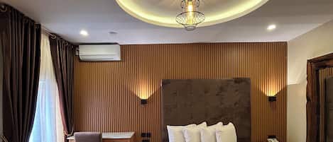 A hotel room with a large bed, a desk, a chair, a ceiling light fixture, and an air conditioning unit.