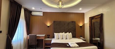 Une chambre d’hôtel avec un grand lit, un bureau, une chaise, un miroir et un luminaire au plafond.