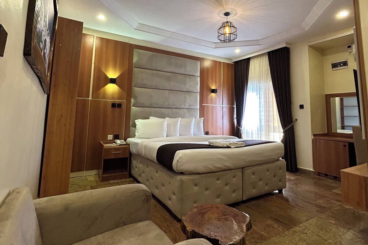 Ein Hotelzimmer mit einem großen Bett, einer Sitzecke mit zwei Sesseln, einem kleinen Tisch, einer Deckenleuchte und einem großen Spiegel.