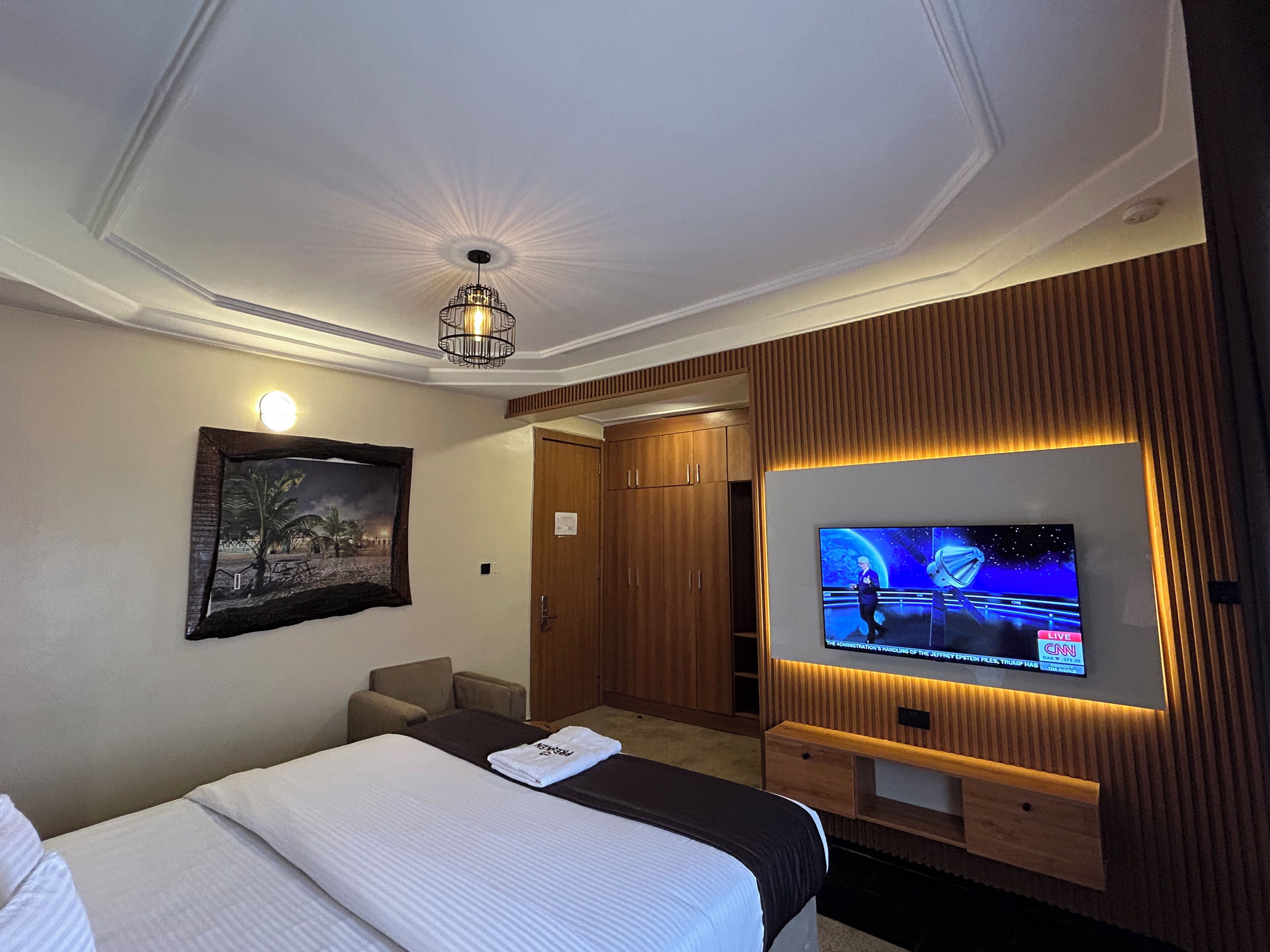 A hotel room with a bed, a television, a framed picture on the wall, and a wooden wardrobe.