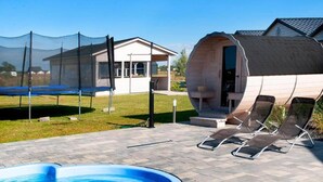 Zona de piscina con trampolín, sillas de descanso y una estructura de madera con techo curvo.