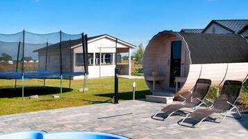 Ein Poolbereich mit Trampolin, Liegestühlen und einer Holzkonstruktion mit gewölbtem Dach.