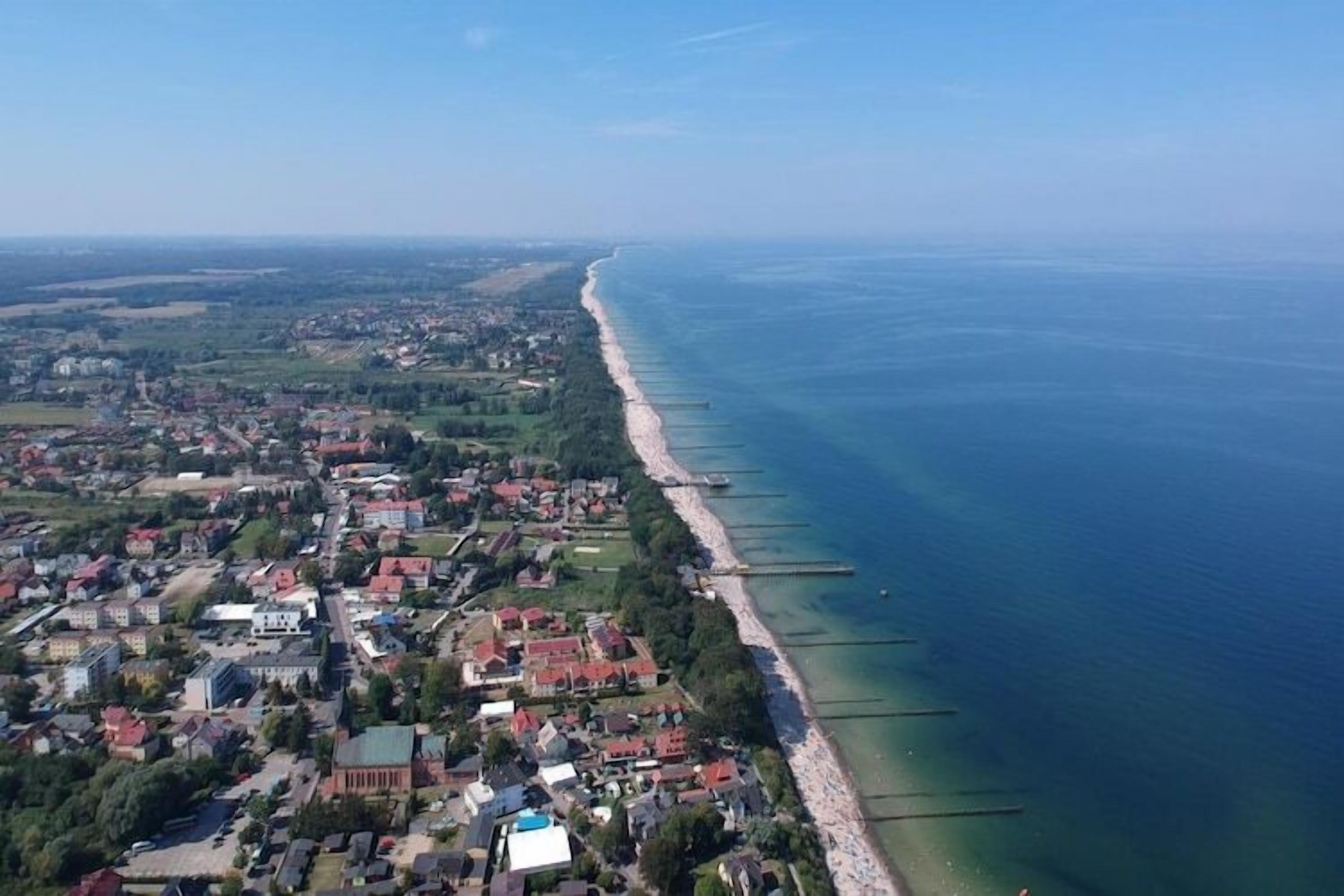 An aerial view of a coastal town with a long beach, clear blue waters, and residential buildings.
