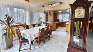 A dining area with a wooden table and chairs, a large clock, and a potted plant. - Holiday villa with sauna, right on the beach (Ustronie Morskie)