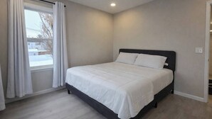 Ein Schlafzimmer mit einem Bett, einem Fenster mit Vorhängen, einem Deckenventilator und einer Lampe.