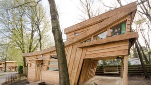 A wooden cabin with a sloped roof, large windows, and a small porch area. - Wooden Lodge Victor de Vos | Slapen in een echte boomhut! (Rijen)
