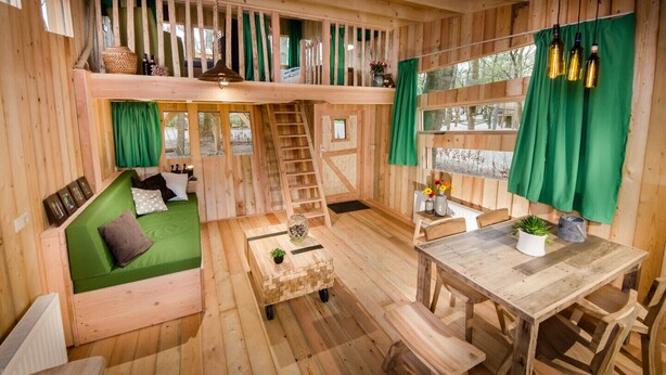 A cozy wooden cabin with a loft bedroom, a dining area, and a small kitchen. - Wooden Lodge Victor de Vos | Slapen in een echte boomhut! (Rijen)
