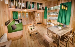 A cozy wooden cabin with a loft bedroom, a dining area, and a small kitchen.