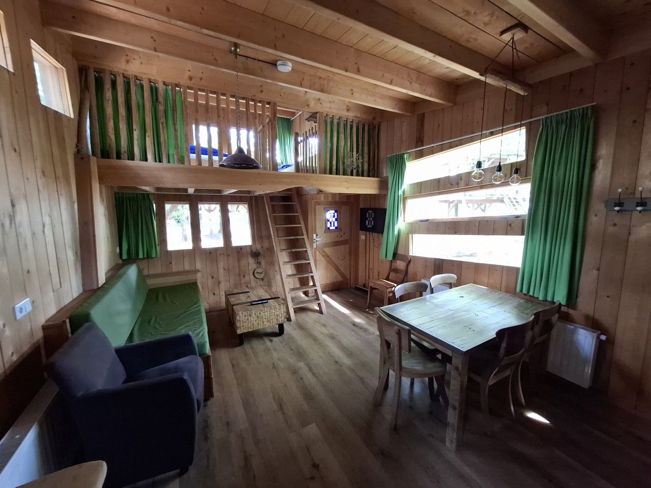 A cabin interior with a loft bed, a dining table, and a staircase to the upper level.
