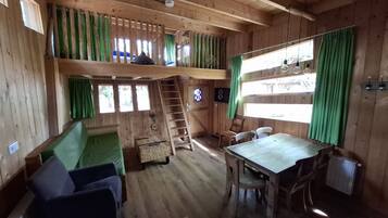 A cabin interior with a loft bed, a dining table, and a staircase to the upper level.