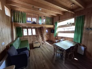Interior de una cabaña con cama en altillo, una mesa de comedor y escalera al nivel superior.
