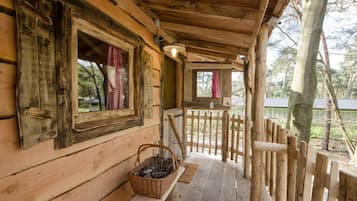 A wooden cabin with a porch, a basket of firewood, and a wooden fence.