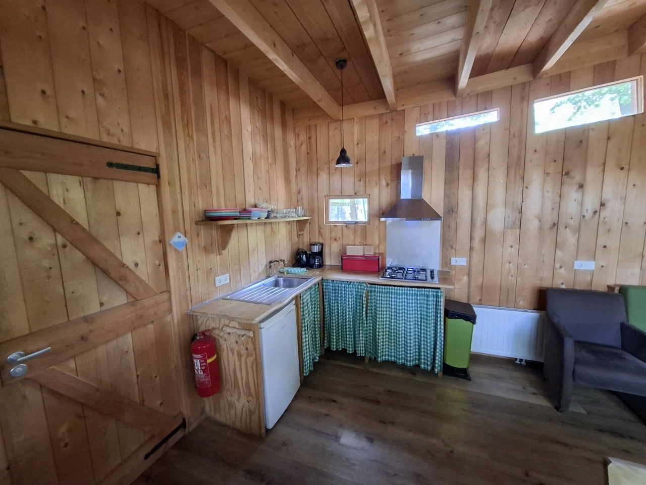 Un intérieur en bois comprenant un coin cuisine, un petit réfrigérateur, un évier, une cuisinière et un extincteur.