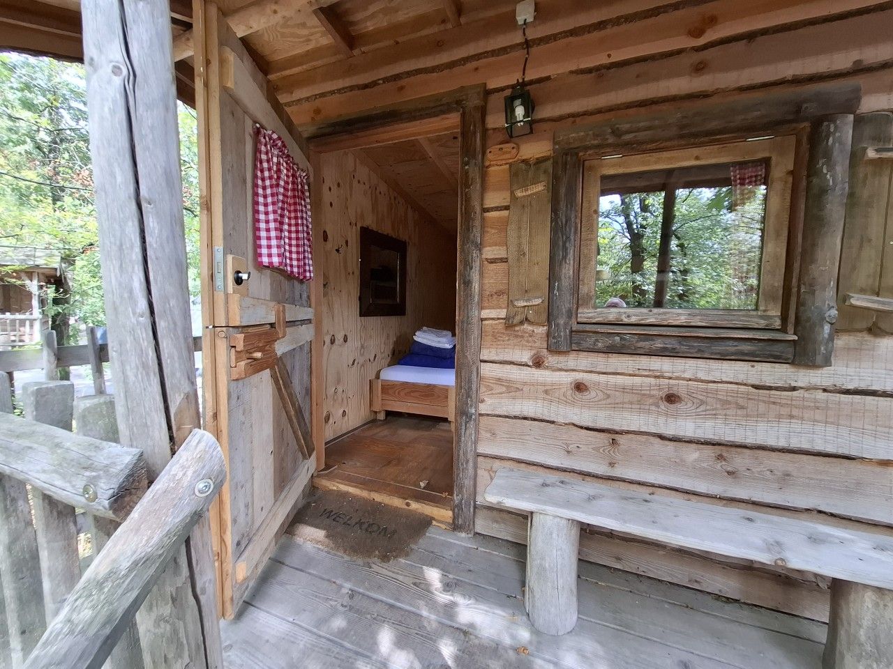 A wooden cabin with a bed, a bench, and a welcome mat.