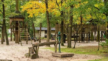 Ein Spielplatz mit Holzelementen, darunter Schaukeln und Klettergerüste, umgeben von Bäumen mit gelben Blättern.