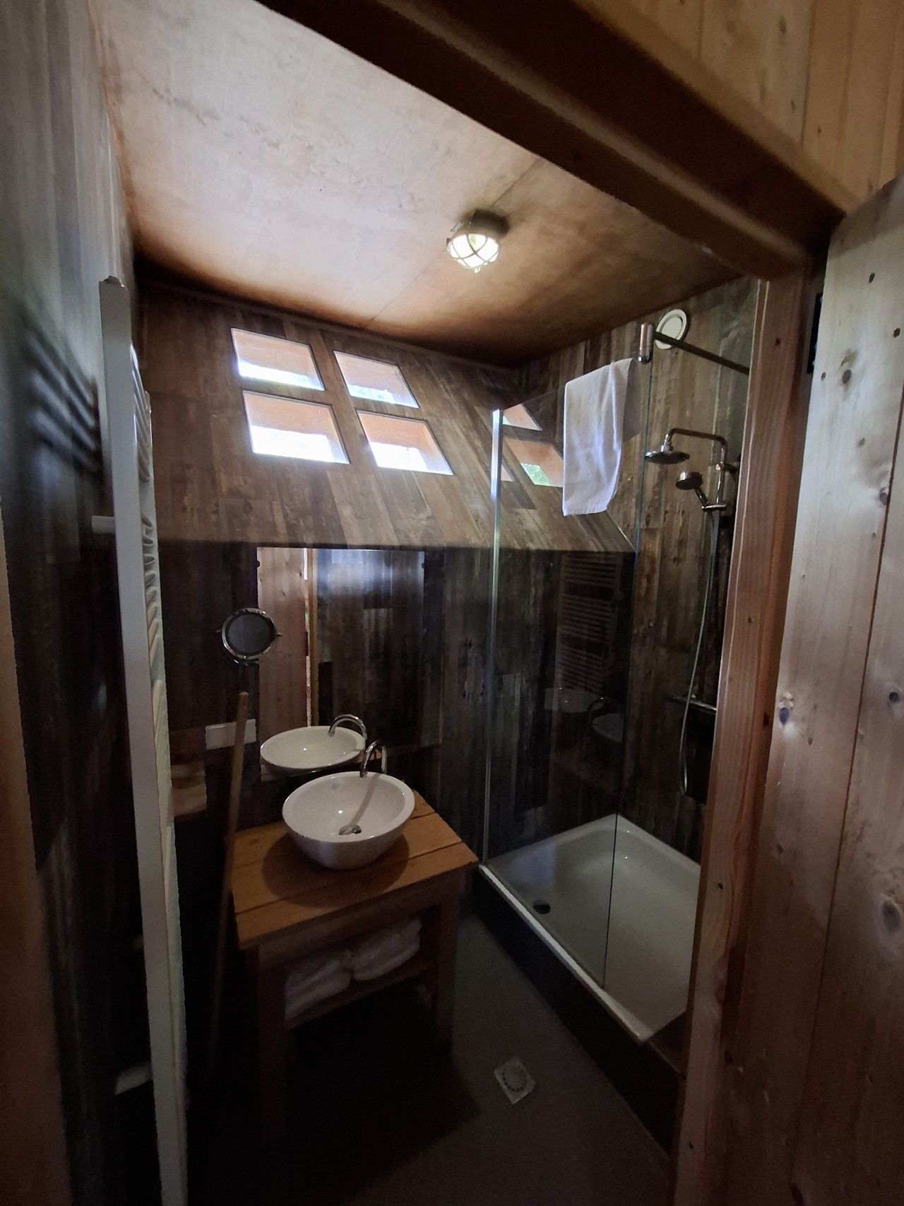 Un baño con paredes de madera, cabina de ducha de vidrio y dos lavamanos.