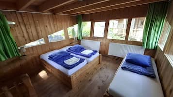 A wooden cabin with a bed, a bench, and a window with curtains.