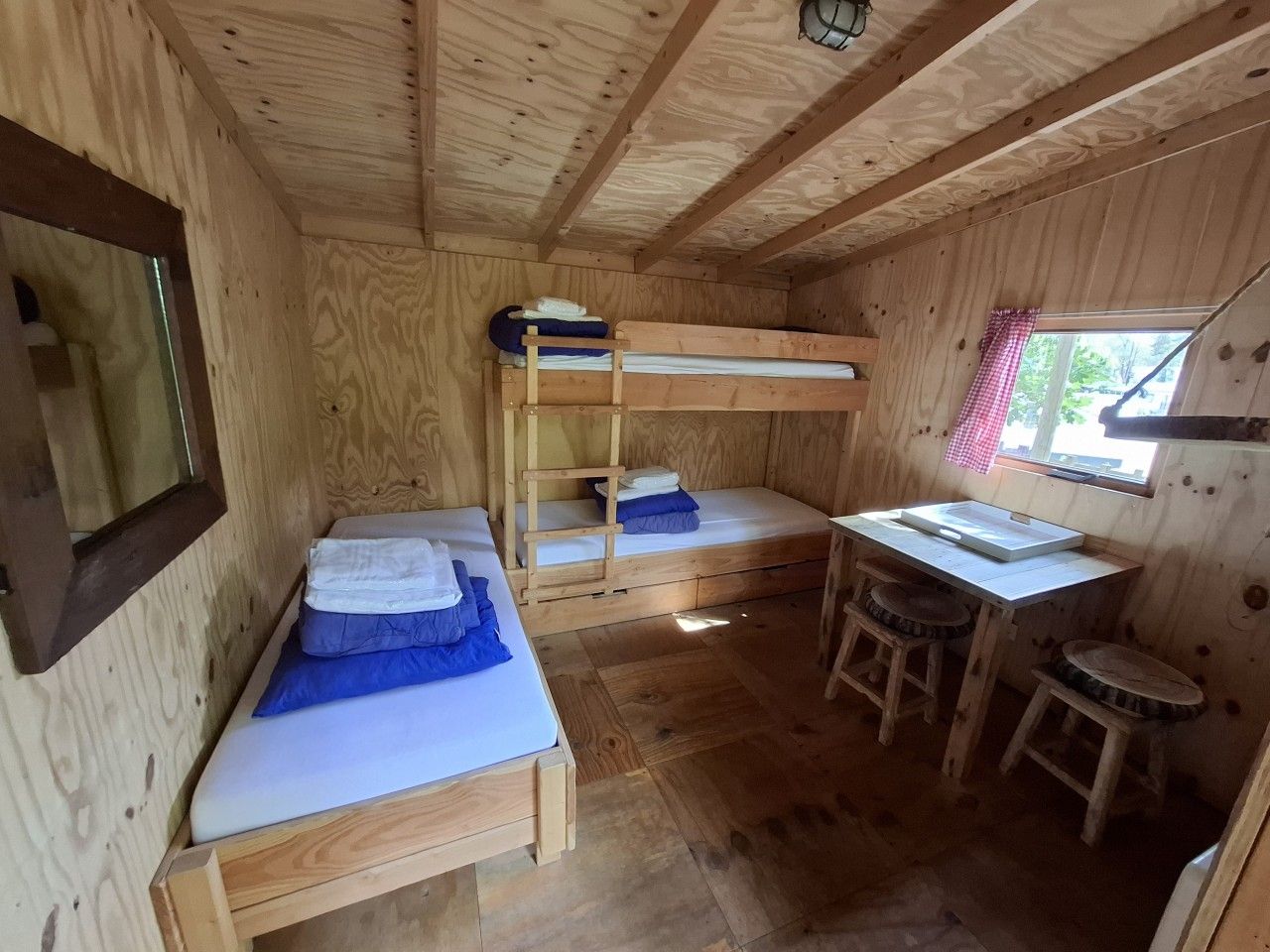 Eine kleine Holzhütte mit Etagenbetten, einem Schreibtisch und einem Fenster.